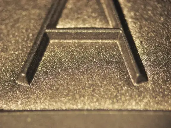 Primer plano de una letra "A" mayúscula en relieve sobre una superficie metálica texturada.