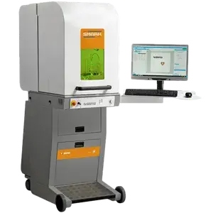 Un aparato de laboratorio con la etiqueta "SHARK" se encuentra junto a un monitor de ordenador que muestra programas informáticos con diagramas técnicos.