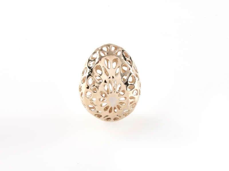 Objeto decorativo en forma de huevo con un intrincado diseño floral calado, fotografiado sobre un fondo blanco liso.