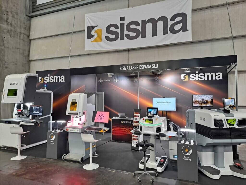 Stand de Sisma Laser España SLU en la 31ª BIEMH 2022, con máquinas láser industriales, pantallas de demostración y señalización de marca sobre un elegante fondo negro.