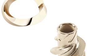 Un anillo de oro liso y un pequeño objeto metálico con ranuras intrincadas, colocados sobre un fondo blanco.