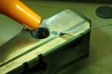 Cordon en soldadura Primer plano de una pistola de calor que se utiliza para aplicar calor a un componente metálico sujetado en un bloque metálico de tornillo de banco, con un alambre colocado cerca.