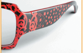 Marco de gafas elegante con diseño de naipes negros y rojos, que presenta palos como corazones, diamantes, tréboles y espadas en un patrón decorativo.