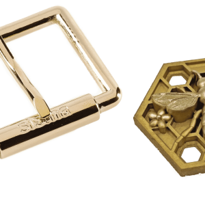 Hebilla de cinturón rectangular dorada junto a un medallón hexagonal con diseño de abeja.