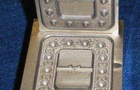 Un molde de metal con patrones intrincados y diseños circulares, mostrado abierto sobre una superficie azul.