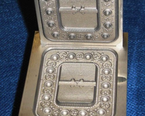 Un molde de metal detallado para crear diseños intrincados, que se muestra abierto, con una cavidad rectangular y patrones ornamentados.