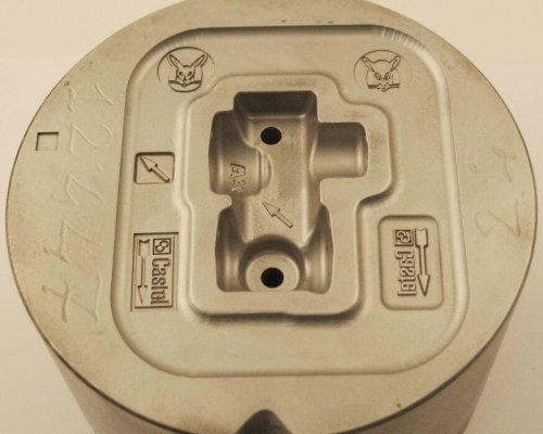Primer plano de un molde de metal con logotipos y símbolos grabados, incluidas flechas, un conejo y la palabra "Castel".