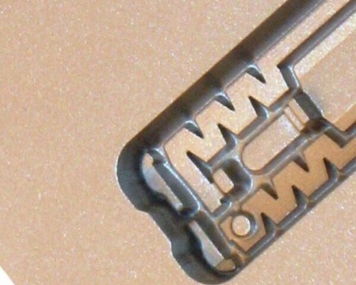 Primer plano de un elemento metálico con intrincados recortes, sobre un fondo de color tostado o beige.