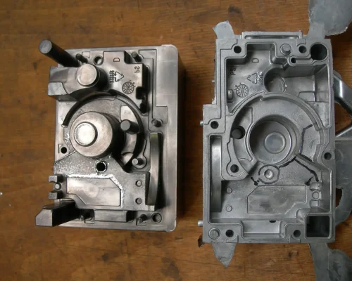 Dos piezas de máquina metálicas con diseños intrincados, que recuerdan moldes elaborados con precisión, se colocan sobre una superficie de madera.