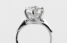 Anillo de plata con un gran diamante redondo engastado en cuatro puntas, sobre un fondo blanco liso.