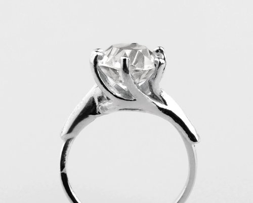 Anillo de plata con un gran diamante redondo engastado en cuatro puntas, sobre un fondo blanco liso.