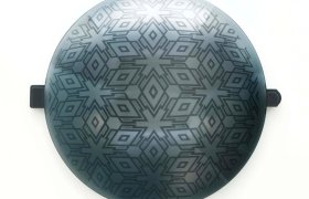 Objeto metálico de forma redonda con motivos geométricos, que presenta dos pequeñas asas en lados opuestos.