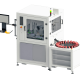 Máquina industrial automatizada con zona de procesamiento cerrada, mesa giratoria con soportes rojos y estación de trabajo informática lateral sobre fondo blanco.