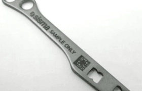 Un soporte metálico alargado con el texto "sisima SAMPLE ONLY" y un código QR, con orificios en ambos extremos, se muestra sobre un fondo liso.