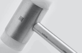 Un mazo plateado con una cabeza de goma blanca y un mango de madera sobre un fondo gris claro.