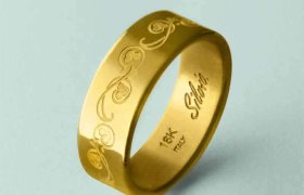 Anillo de oro con diseño de espiral grabado, con la inscripción "18K Italia" y "Silvia". Fondo azul pálido.
