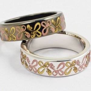 Dos anillos entrelazados con diseños de mariposas en rosa y dorado sobre bandas metálicas sobre un fondo blanco liso.