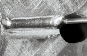 Primer plano de una superficie metálica con un tornillo parcialmente insertado, mostrando líneas y texturas grabadas visibles.