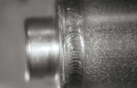Primer plano de un tubo de metal con textura de soldadura detallada, que muestra ranuras finas y una superficie cilíndrica lisa.