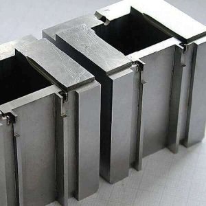 Primer plano de bloques de precisión metálicos con diseño entrelazado sobre una superficie con patrón de cuadrícula.