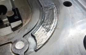 Primer plano de una superficie metálica con un arco ranurado y dos agujeros, junto a una pequeña hendidura circular y compartimentos rectangulares, que encarna la esencia de la Industria 4.0—un punto de inflexión hacia el futuro de la fabricación.