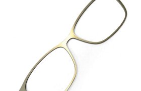 Montura de gafas fina y rectangular con acabado metálico, fotografiada sobre un fondo blanco.