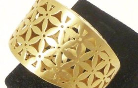 Pulsera de oro con diseño floral recortado, exhibida sobre un soporte negro.