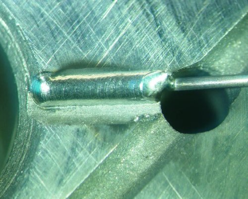 Primer plano de una superficie metálica que muestra un pasador cilíndrico insertado en una ranura mecanizada junto a un orificio circular, con el contacto de la herramienta visible.
