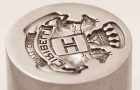 Sello de metal con escudo grabado que muestra una "H" central, rematada por una corona, y el texto "MONTE CARLO" y "LISTE GIN".