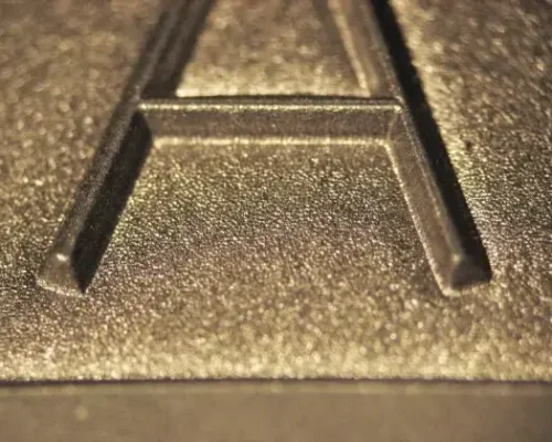 Primer plano de una letra "A" mayúscula en relieve sobre una superficie metálica texturada.