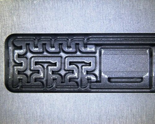 Primer plano de un laberinto de plástico negro incrustado en una superficie metálica rectangular plateada.