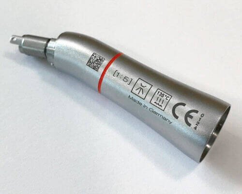 Una pieza de mano dental plateada con marcas técnicas y un código QR en el lateral, colocada sobre un fondo blanco liso.
