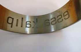 Pieza de metal curvada con la inscripción "Pilar 266" recortada al revés, colocada sobre una superficie blanca.