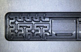 Primer plano de un intrincado patrón geométrico grabado en una superficie metálica, con líneas y formas interconectadas.