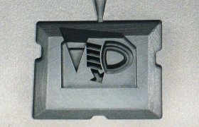 Primer plano de una superficie metálica con un diseño geométrico abstracto empotrado, con formas y líneas angulares, centrado dentro de la imagen.