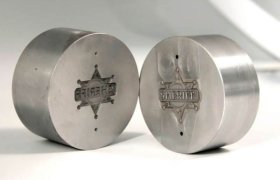 Dos objetos metálicos redondos con insignias de estrella de sheriff grabadas. Una insignia dice "SHERIFF" y la otra es de espejo. Sobre un fondo neutro.