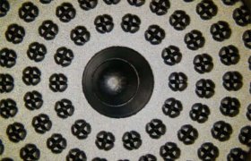 Primer plano de un patrón circular con un círculo negro central rodeado de círculos más pequeños, cada uno de los cuales contiene un diseño en forma de cruz.