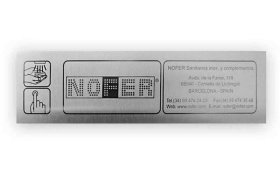 Una placa metálica rectangular con la marca "NOFER" en puntos y datos de contacto. Incluye un icono de botón táctil con la ilustración de una mano señalando.