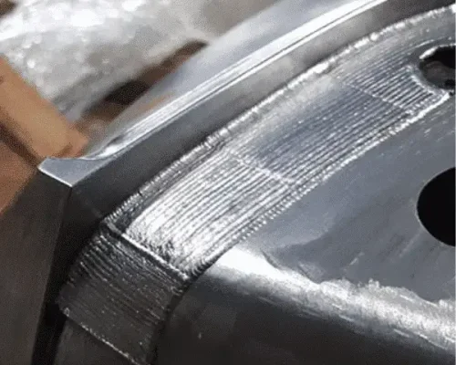 Primer plano de una superficie metálica con marcas visibles de cordones de soldadura y un borde mecanizado, mostrando diferentes texturas superficiales.