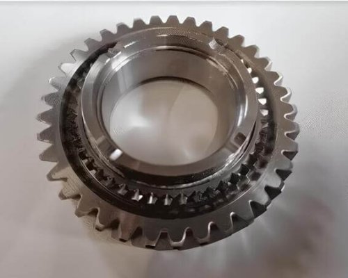 Un engranaje metálico con dientes espaciados uniformemente descansa sobre una superficie de color claro, mostrando un mecanizado detallado y un diseño circular.