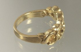 Anillo de oro con un diseño intrincado, que presenta un patrón en espiral y un pequeño detalle circular sobre una superficie reflectante.