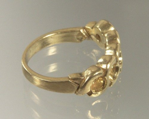 Anillo de oro con un diseño intrincado, que presenta un patrón en espiral y un pequeño detalle circular sobre una superficie reflectante.