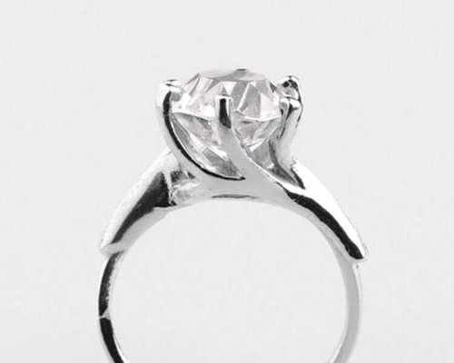 Anillo de plata con un gran diamante de talla redonda engastado en garras, expuesto sobre un fondo liso.