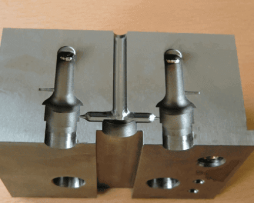 Un molde de metal con dos cavidades cilíndricas paralelas y detalles intrincados sobre un fondo plano.