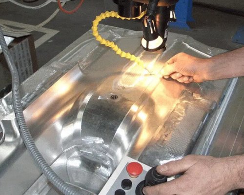 Una persona maneja una máquina herramienta utilizando un joystick y botones para inspeccionar o trabajar en un componente metálico de gran tamaño bajo una iluminación focalizada.
