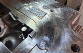 Primer plano de un molde metálico con aspecto desgastado, que muestra una herramienta en el borde superior y varias ranuras y sujetadores visibles en la superficie, marcando un punto de inflexión hacia el futuro de la fabricación.